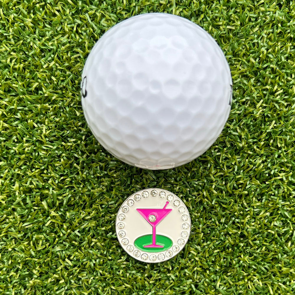 golf ball on grass with a pink martini-themed ball marker