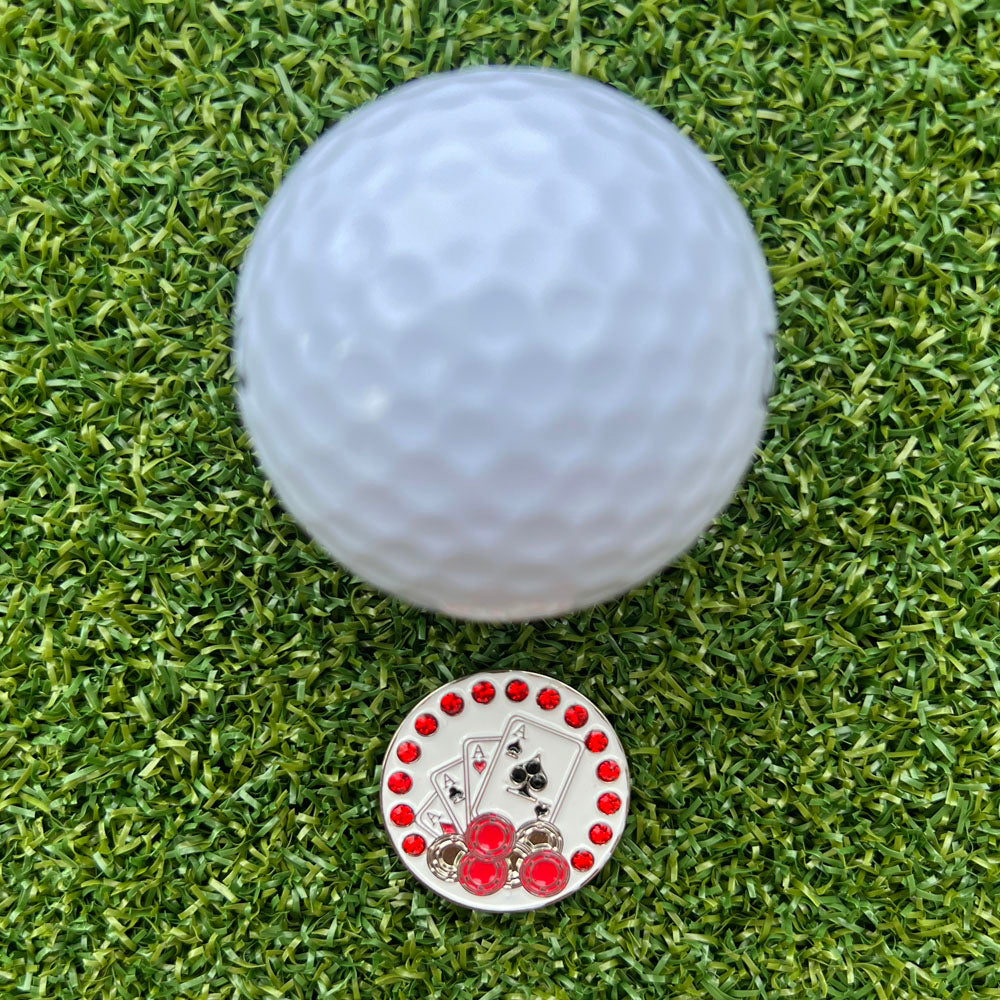Golf ball on green grass with a decorative golf ball marker featuring playing card symbols.