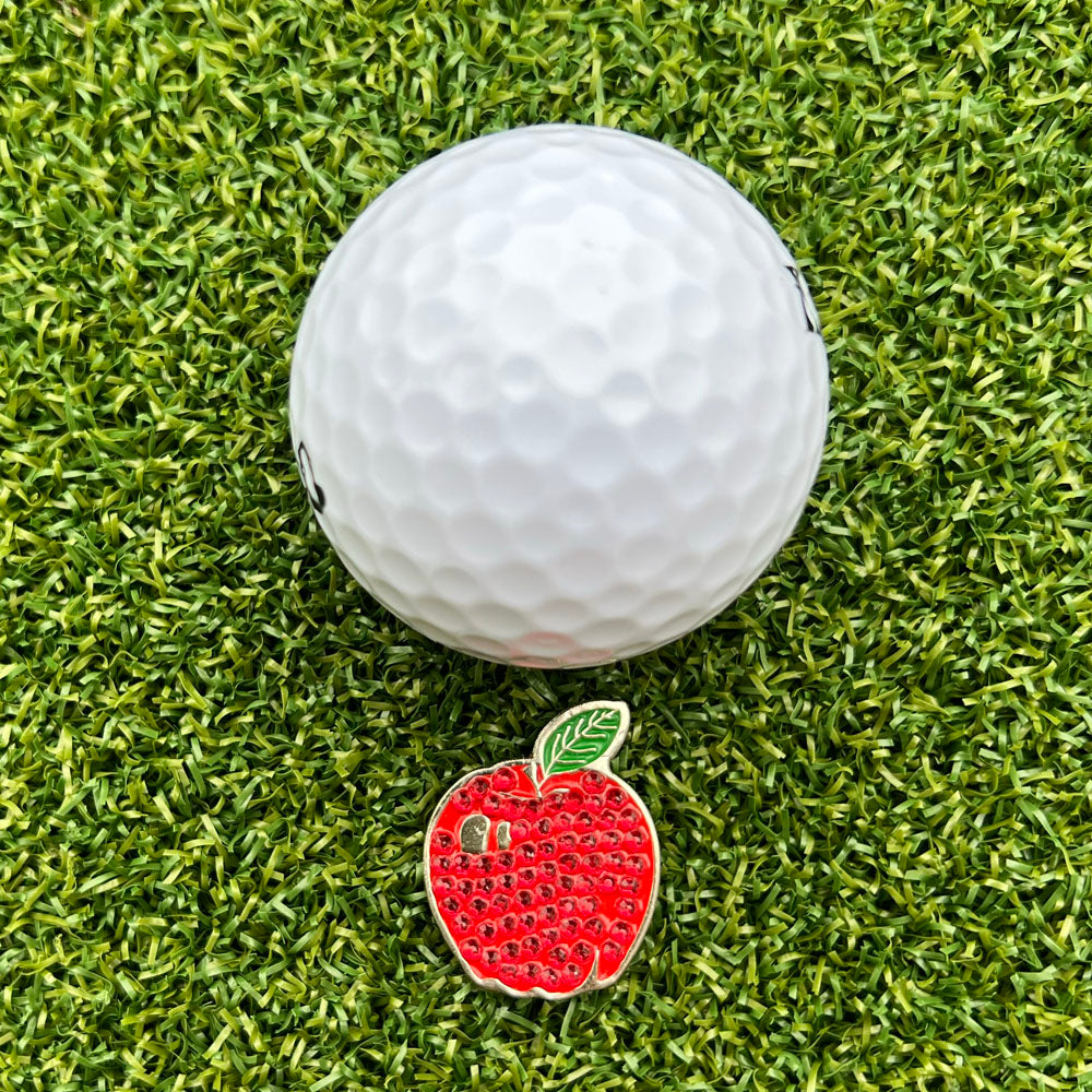 Golf ball on grass with a red apple-shaped ball marker