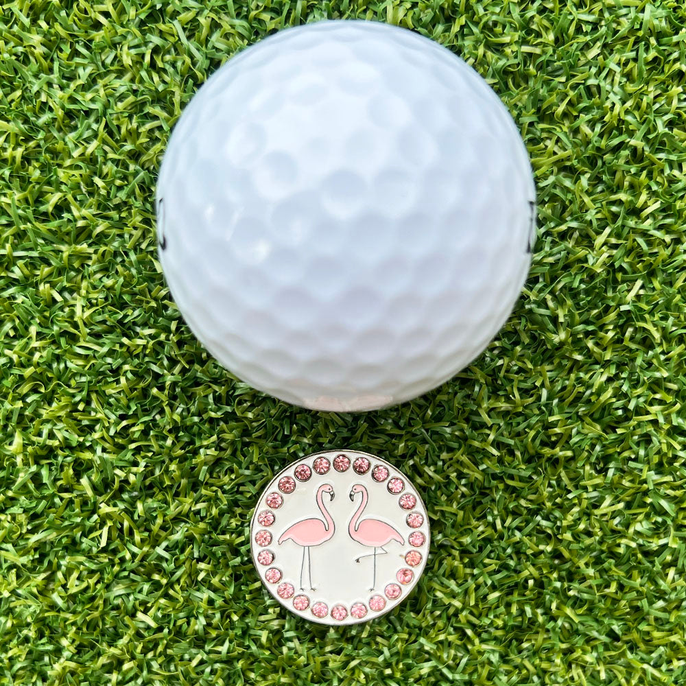 Golf ball on grass with a pink flamingo-themed golf ball marker.