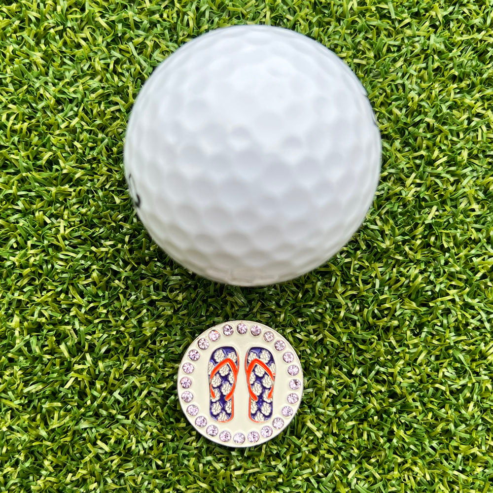 Golf ball on a grass surface with a colorful purple flop flop golf ball marker in front