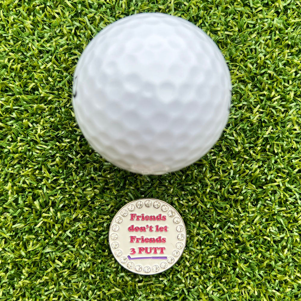 Golf ball on green grass with a golf ball marker reading 'Friends don't let friends 3 PUTT'.