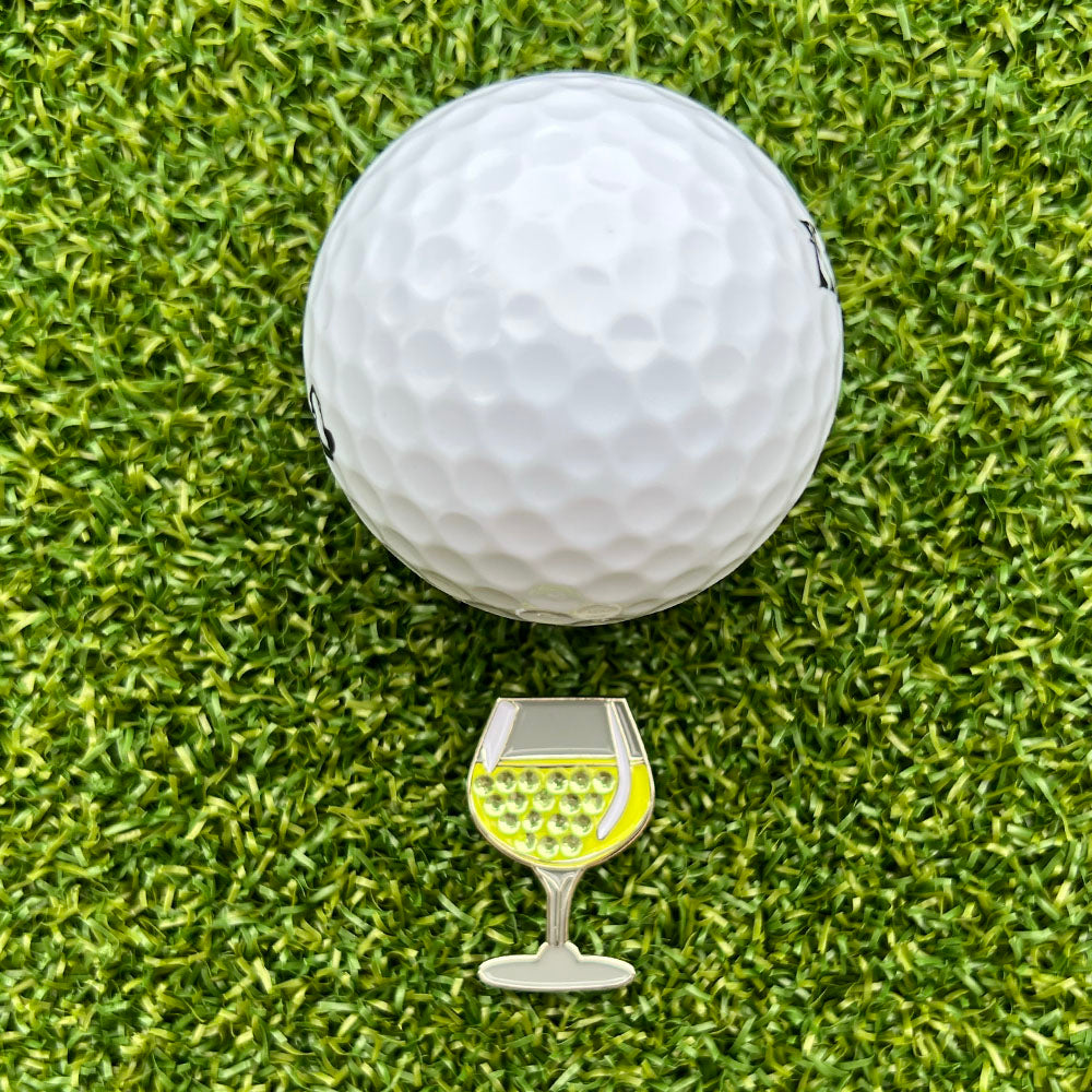 glass of white wine shaped ball marker with white golf ball on grass