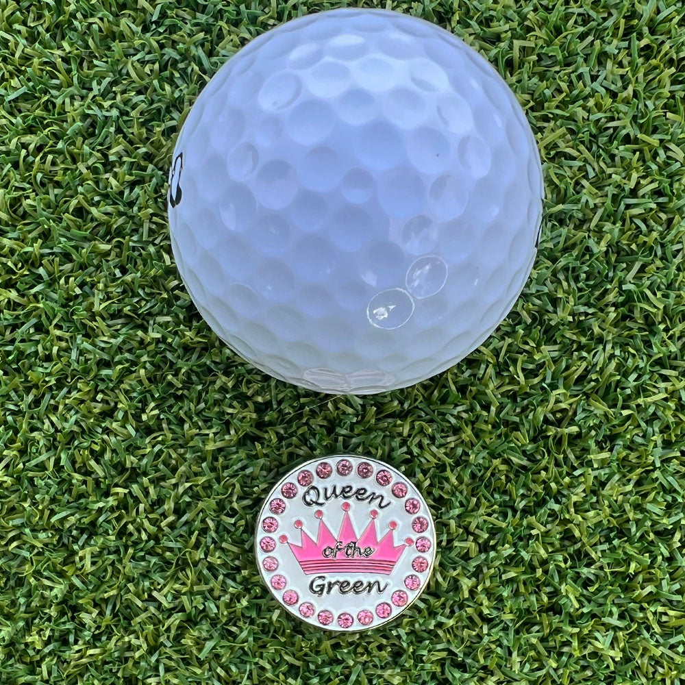 Golf ball on grass with a 'Queen of the Green' (pink text) ball marker