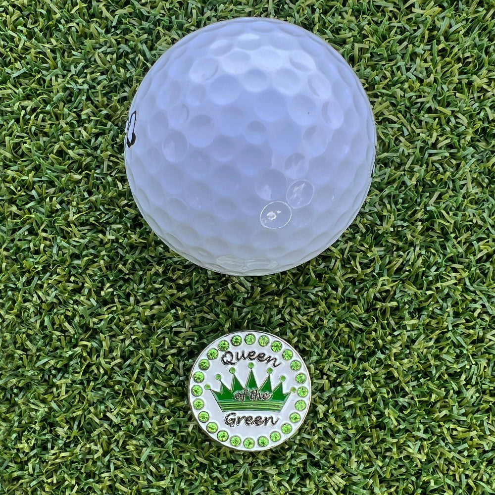 White golf ball on green grass with a 'Queen of the Green' ball marker.