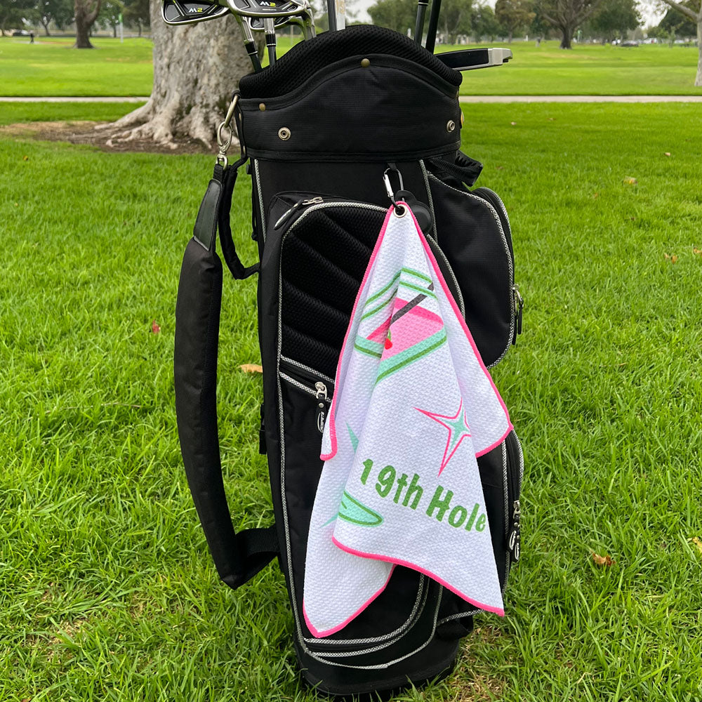 Golf bag with a 19th hole towel hanging out, on a grassy field