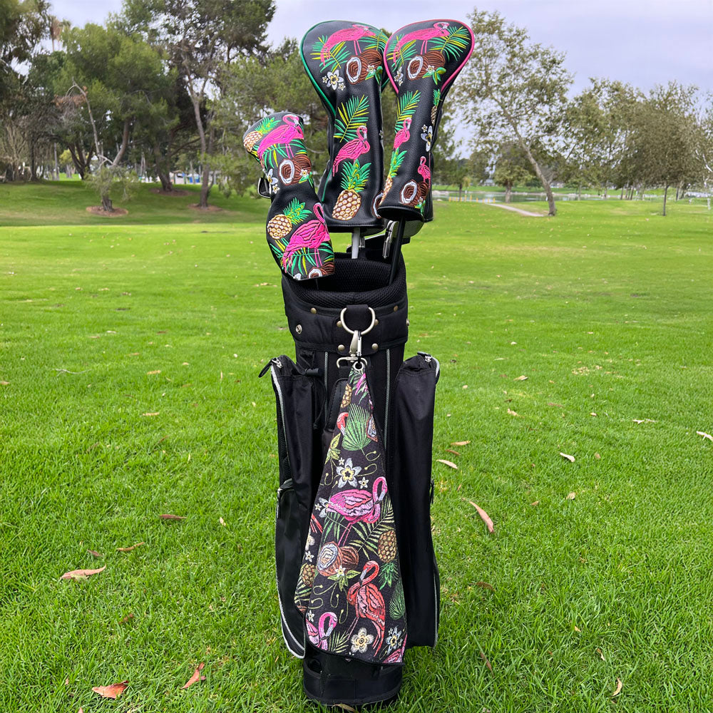 Golf clubs with tropical flamingo & floral designs in a black bag on a grassy field