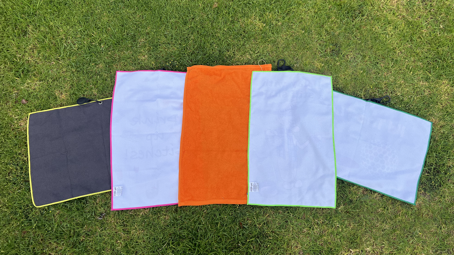 Five colorful golf towels displayed on grass for a limited-time mystery bonus gift promotion.