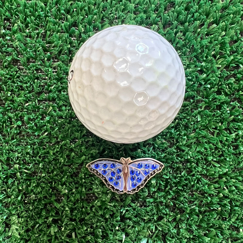 Golf ball with a blue butterfly-shaped metal ball marker on green grass