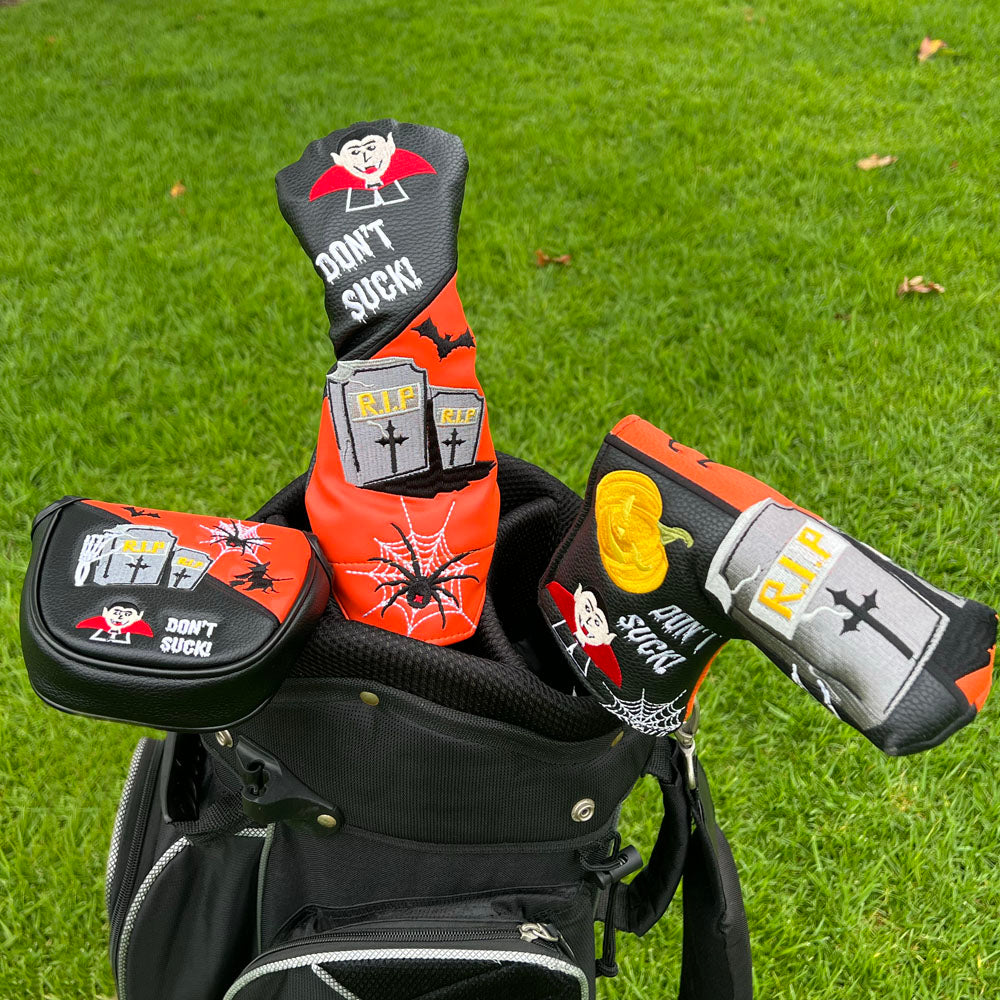 Golf club heads with Halloween-themed covers on a golf bag against a grass background