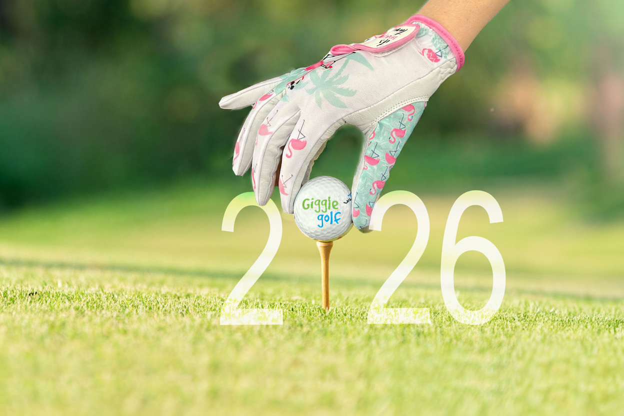 Golf glove with flamingo pattern holding a golf ball on a tee with 2026 on green grass - Giggle Golf accessories