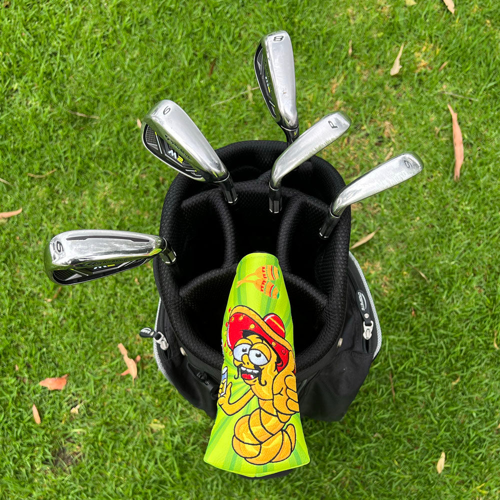 Golf clubs in a bag with a colorful green blade putter cover with embroidered sombrero-wearing worm holding tequila shot and fiesta details on grass