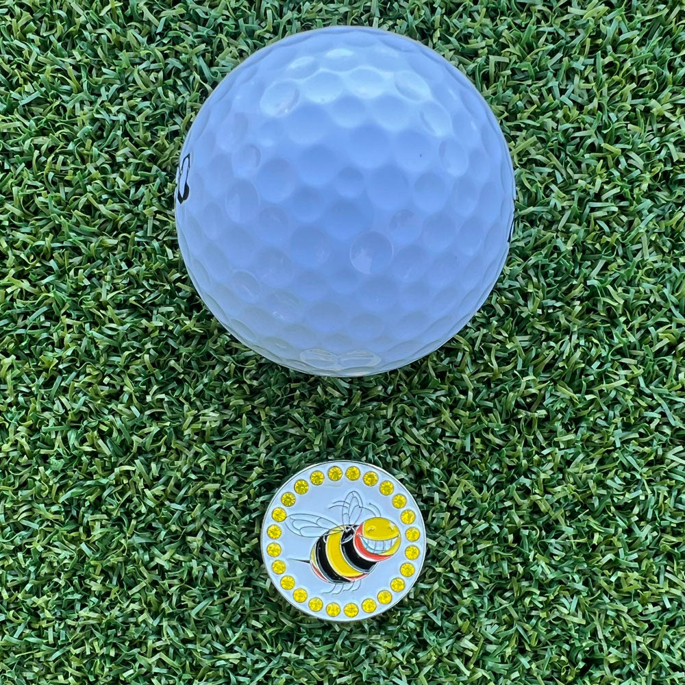 White golf ball on green grass with a bee-themed golf ball marker.