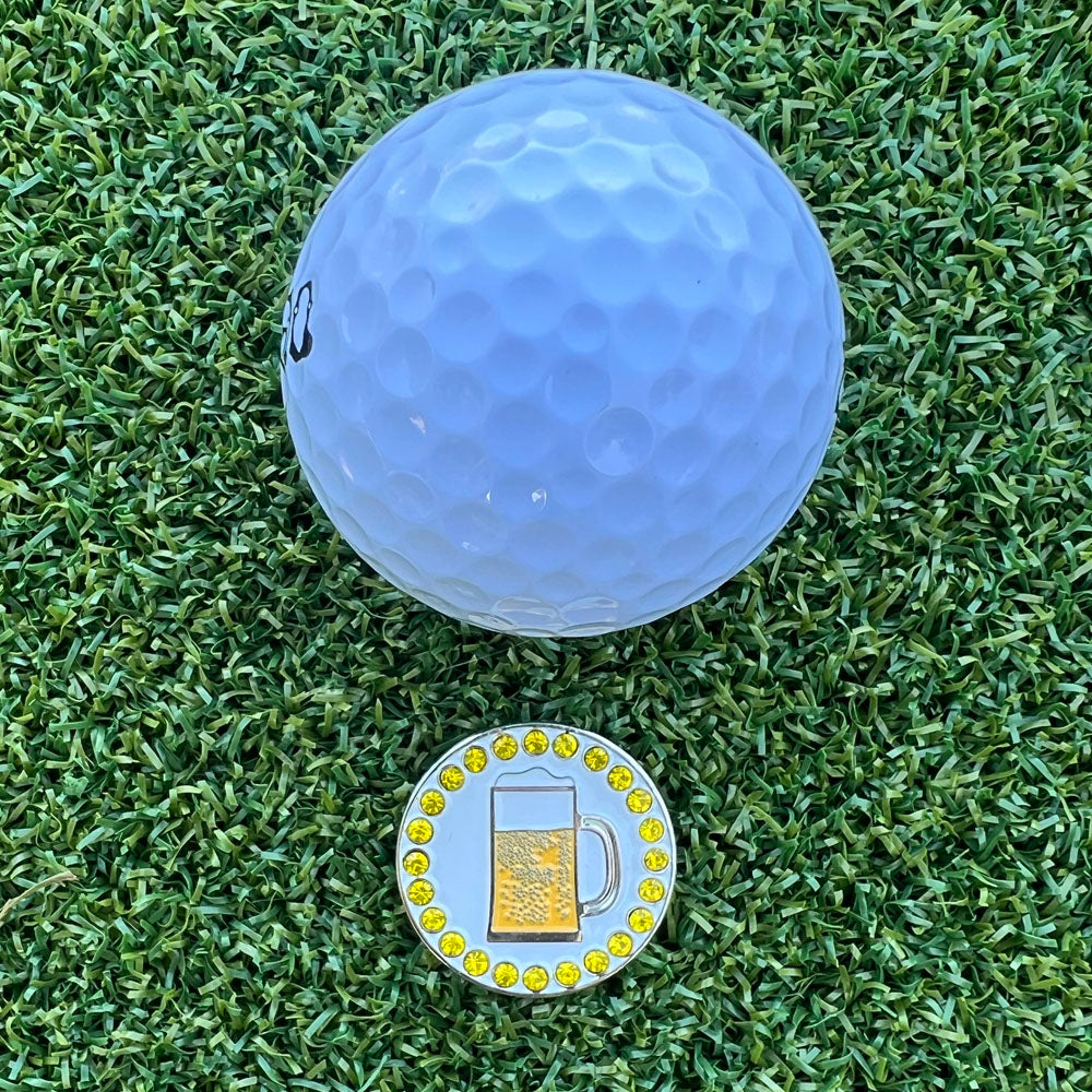Golf ball on grass with a ball marker featuring a beer mug design.