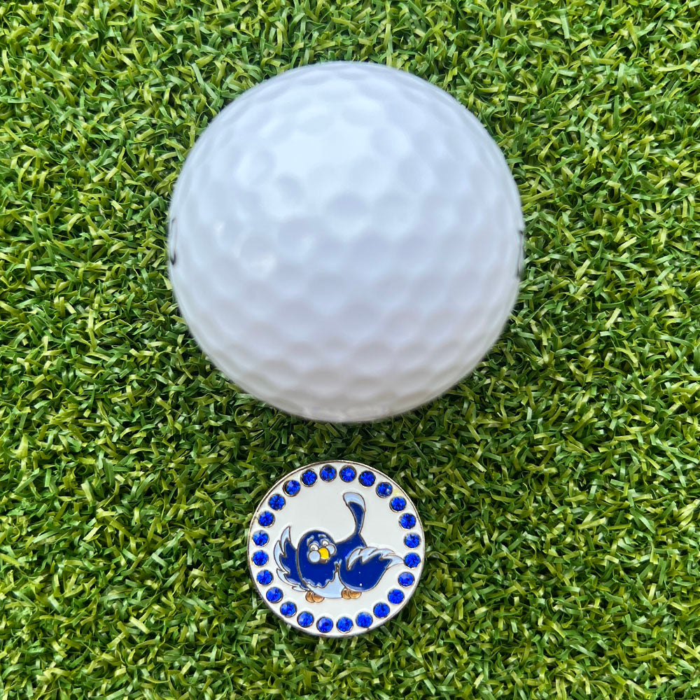 Golf ball on a green grass surface with a decorative golf ball marker featuring a blue bird design.