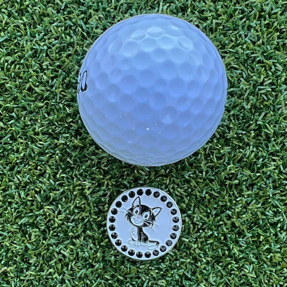 Golf ball and a metal ball marker with a black cat design on grass