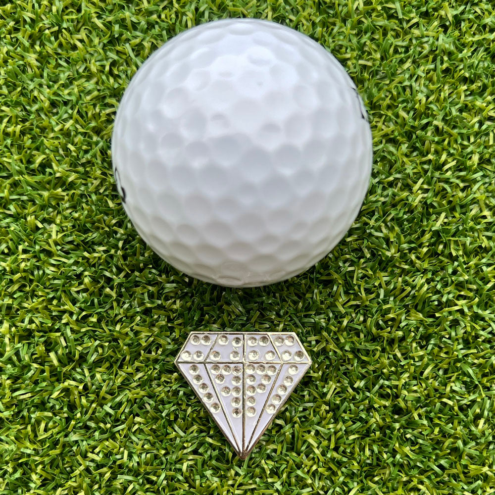 Golf ball on green grass with a decorative white diamond-shaped ball marker
