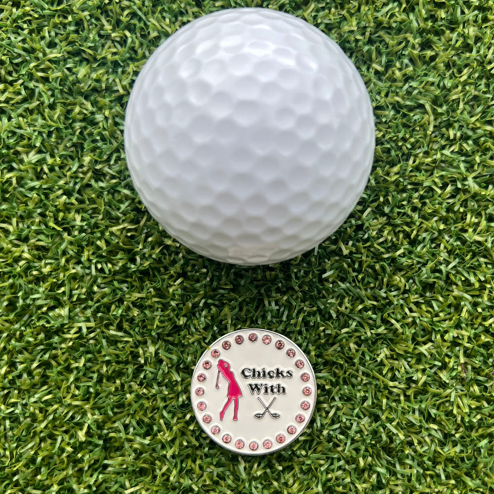 Chicks With Sticks pink and white golf ball marker next to a golf ball on grass