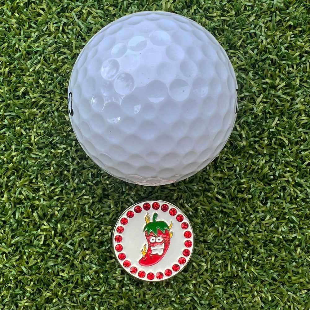 Golf ball and a flaming red chili pepper golf ball marker on green grass