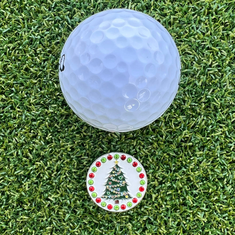 Golf ball on a grassy surface with a Christmas Tree-themed golf ball marker.