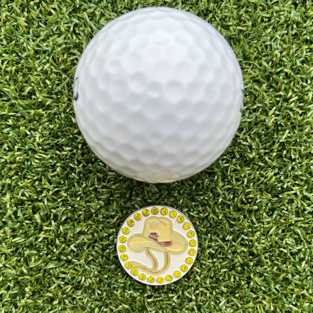 Golf ball and a golf ball marker with a cowboy hat design on grass