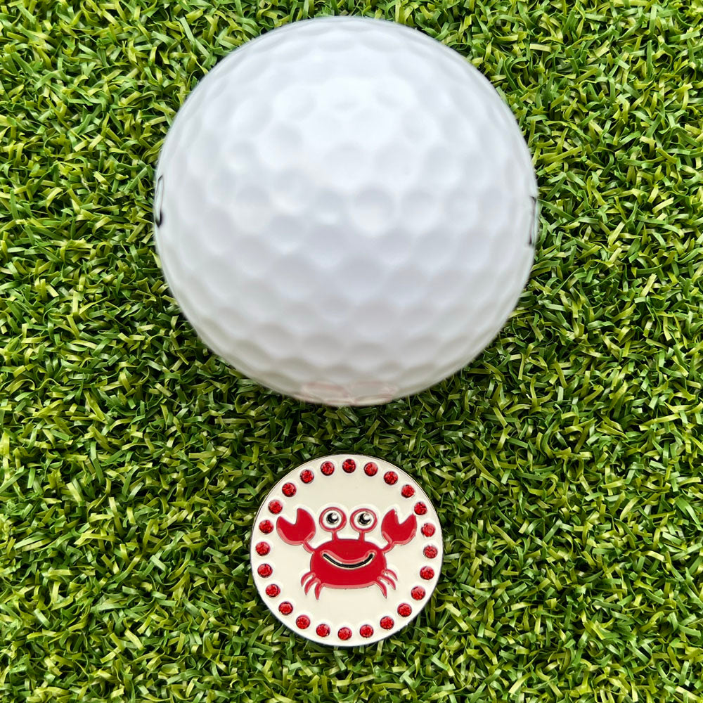 Golf ball on grass with a crab-themed golf ball marker
