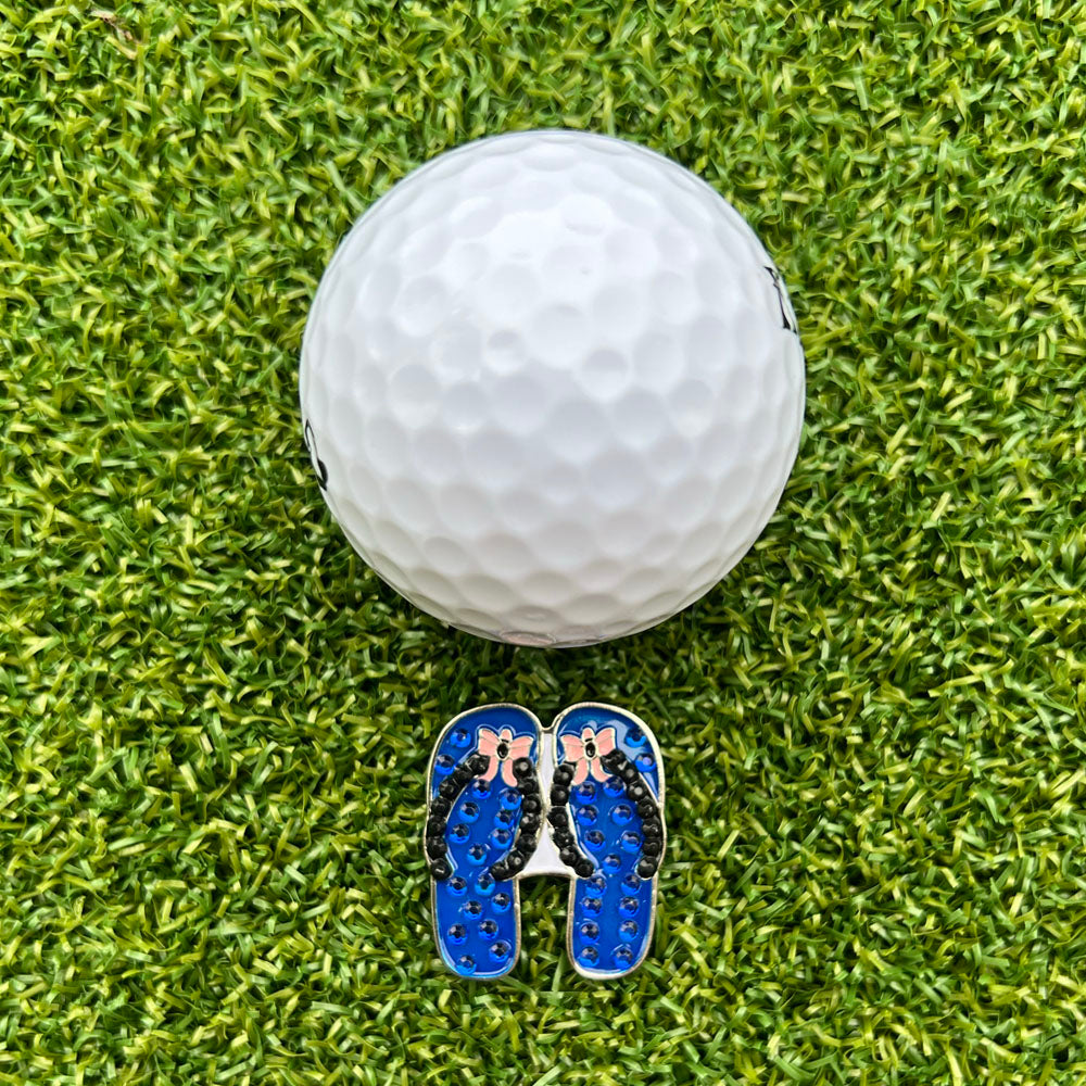 blue flip flop shaped ball marker with white golf ball on grass