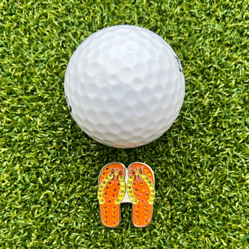 orange flip flop shaped ball marker with white golf ball on grass