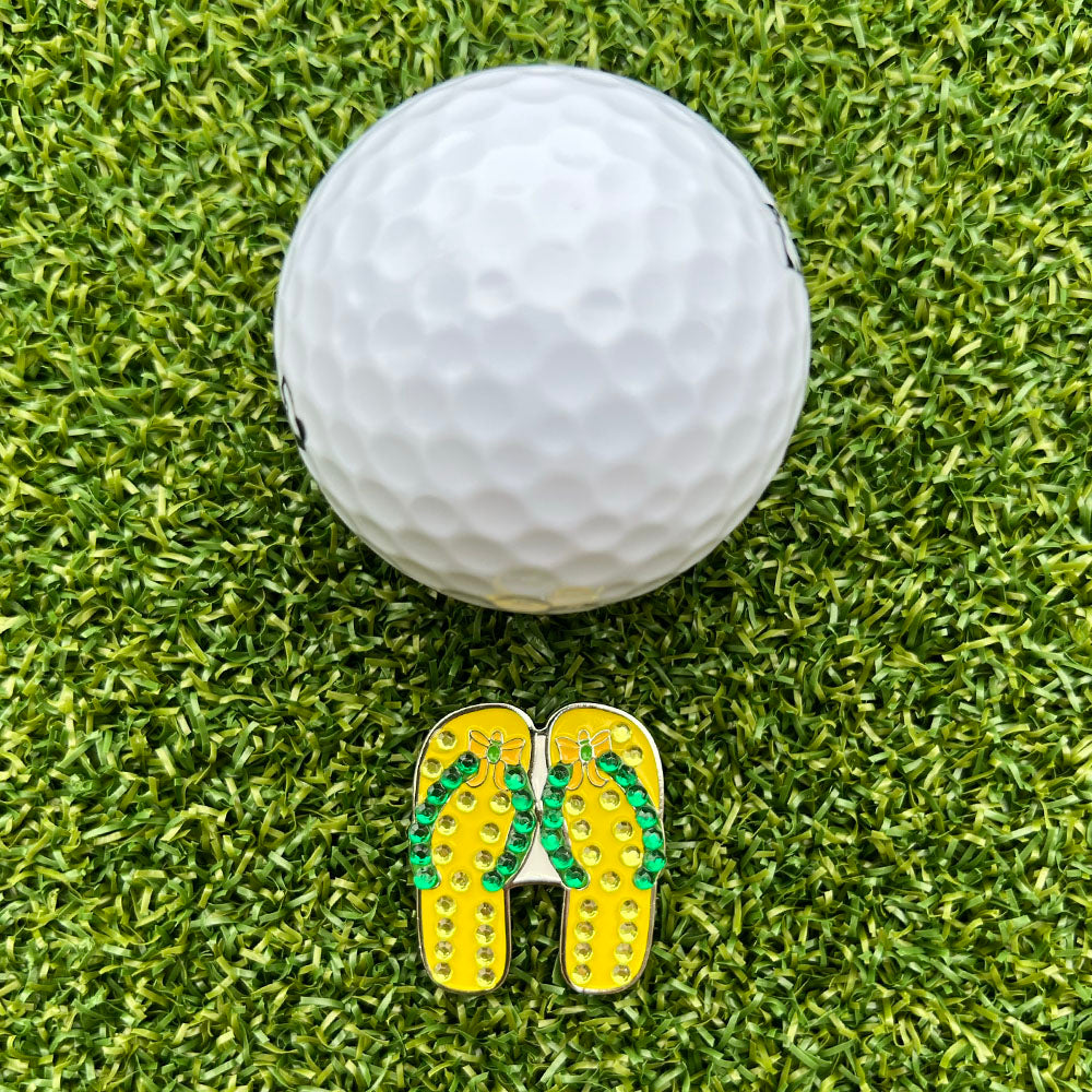 yellow flip flop shaped ball marker with white golf ball on grass