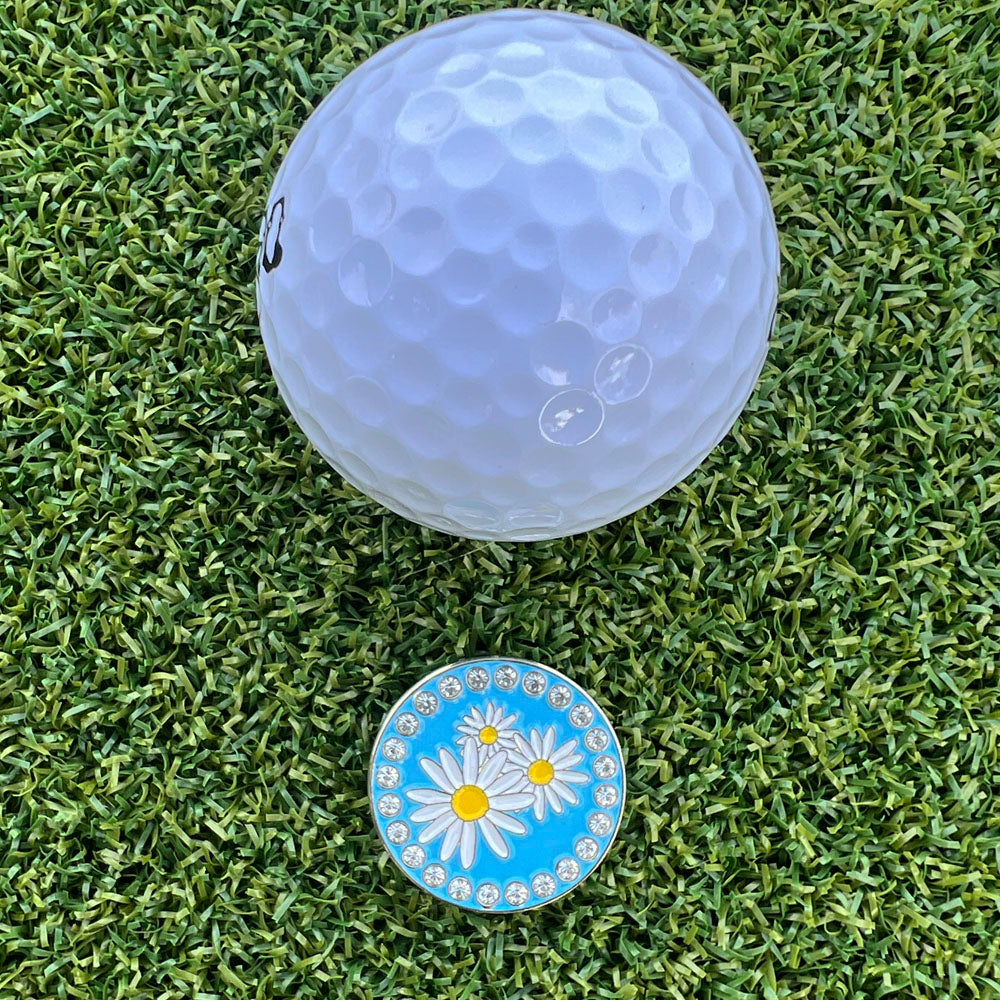 Golf ball on a grass with a golf ball marker featuring a daisy design.