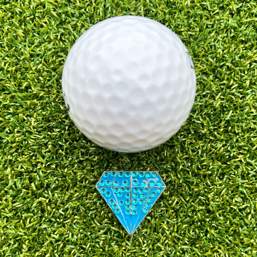 Golf ball on a green grass surface with a blue diamond-shaped ball marker.