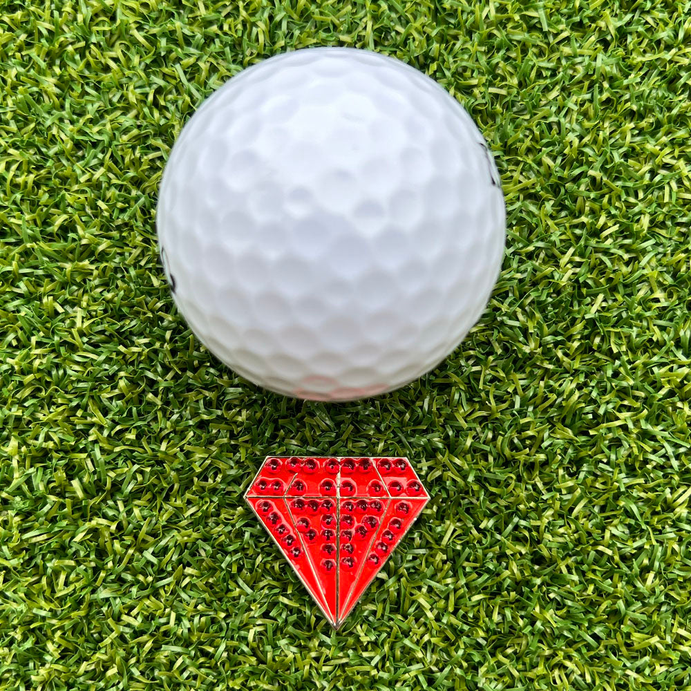 Golf ball on green grass with a red diamond-shaped golf ball marker in front