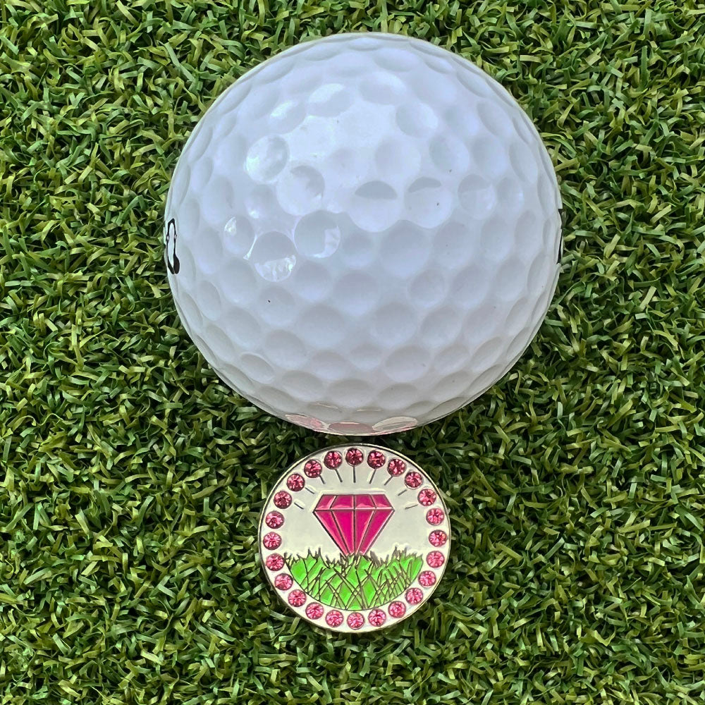 Golf ball with a pink diamond-themed marker on green grass