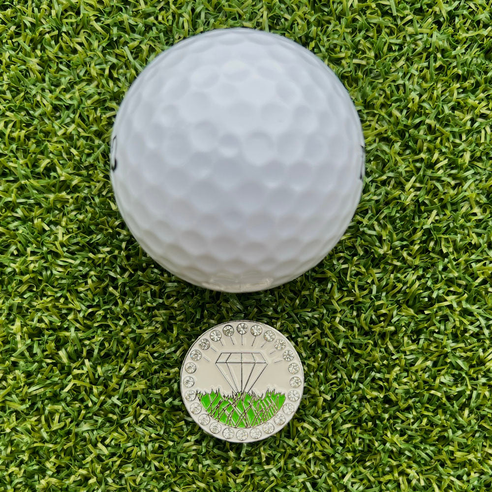 Golf ball on grass with a ball marker featuring diamond in the rough design.