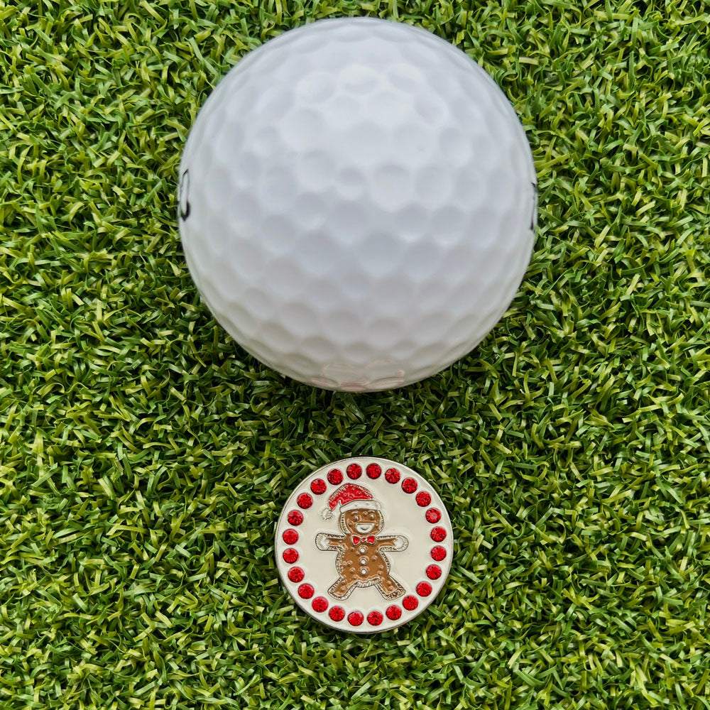 Golf ball on a green grass surface with a decorative golf ball marker featuring a gingerbread man design.