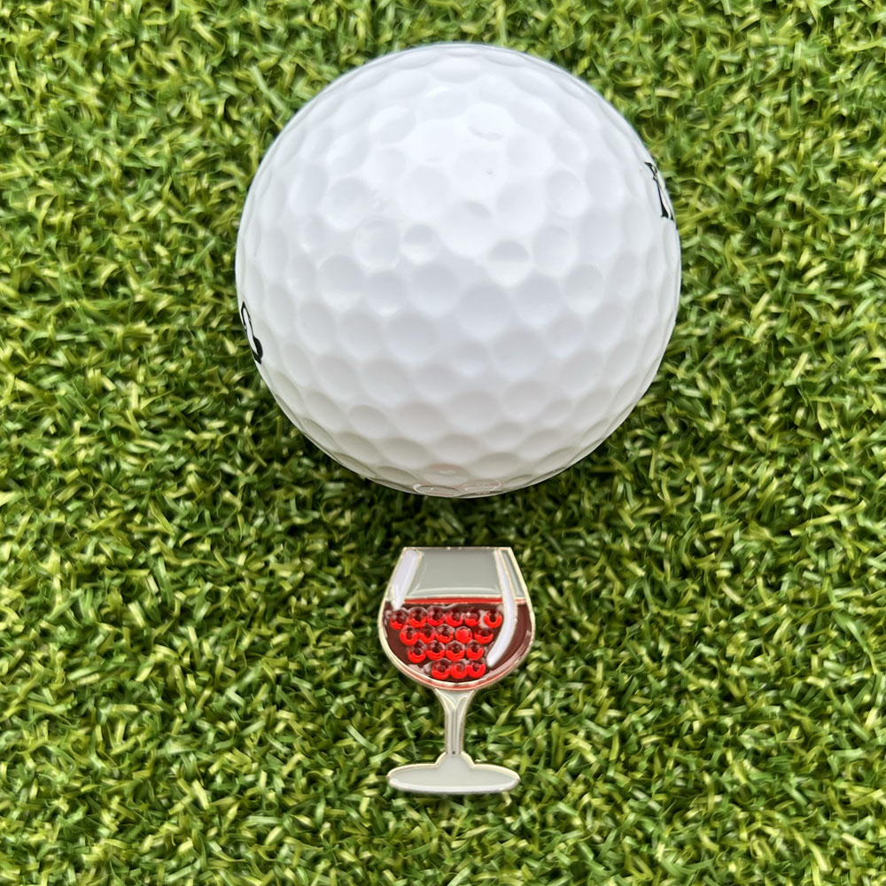 glass of red wine shaped ball marker with golf ball on grass