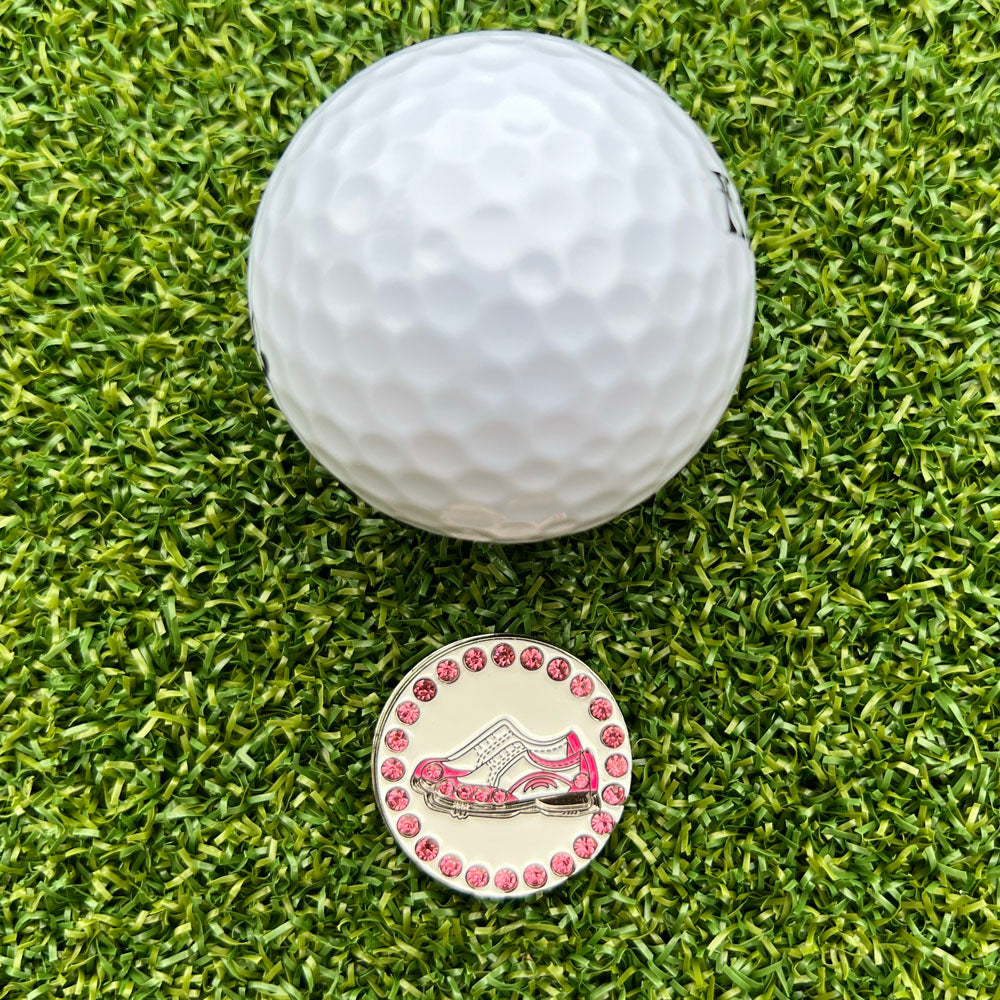 Golf ball and decorative golf ball marker with a pink and white shoe design on green grass