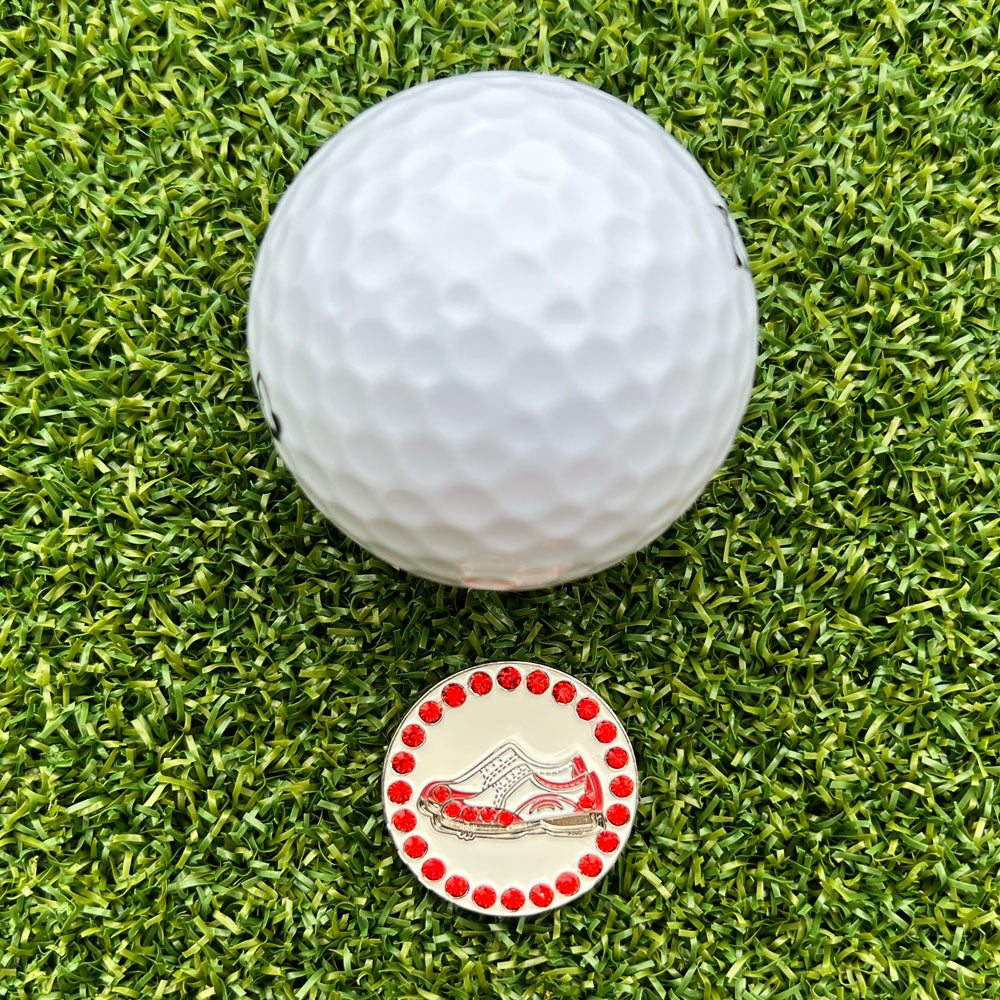 Golf ball on a grassy surface with a golf marker featuring a red and white shoe design.