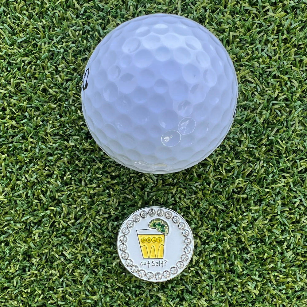 Golf ball and tequila shot ball marker on a grassy surface