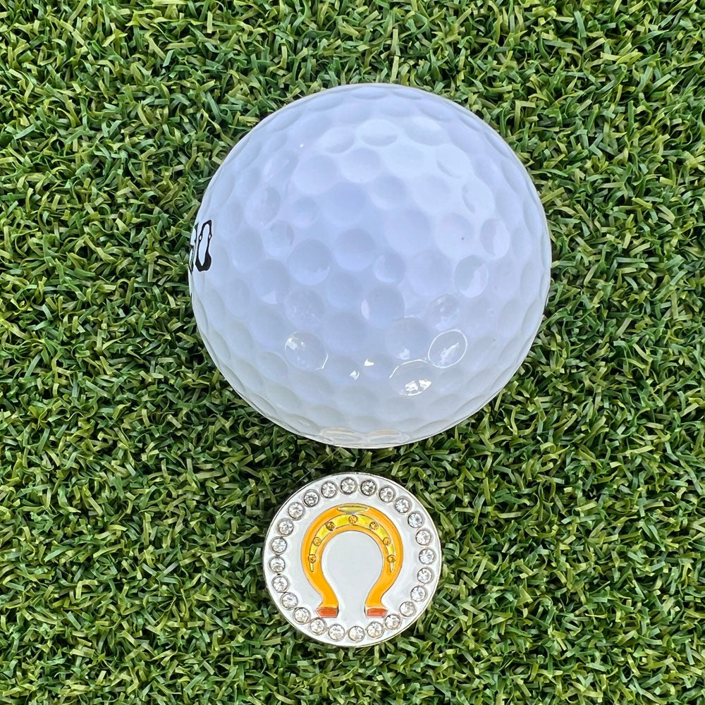 Golf ball on a grass surface with a golden horseshoe golf ball marker.