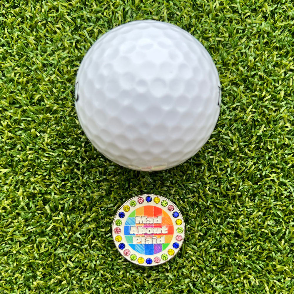 Golf ball on grass with a colorful 'Mad About Plaid' bling ball marker