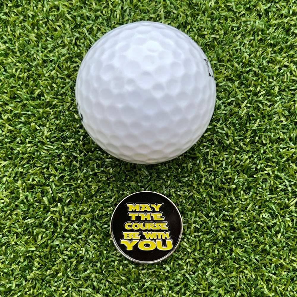 golf ball on grass with black ball marker with 'May The Course Be With You' yellow text