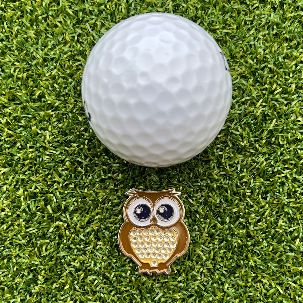 Golf ball on grass with an owl-shaped golf ball marker in front