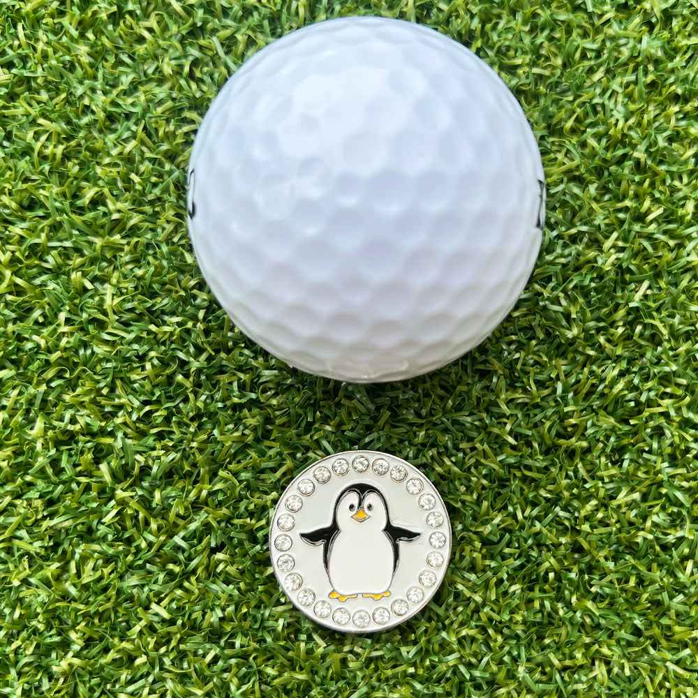 Golf ball on a green grass surface with a penguin-themed golf ball marker.