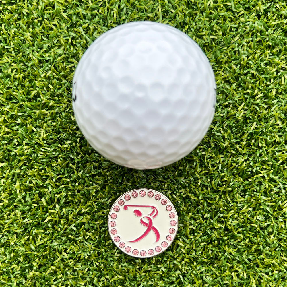 Golf ball on a green grass surface with a pink and white golf ball marker.
