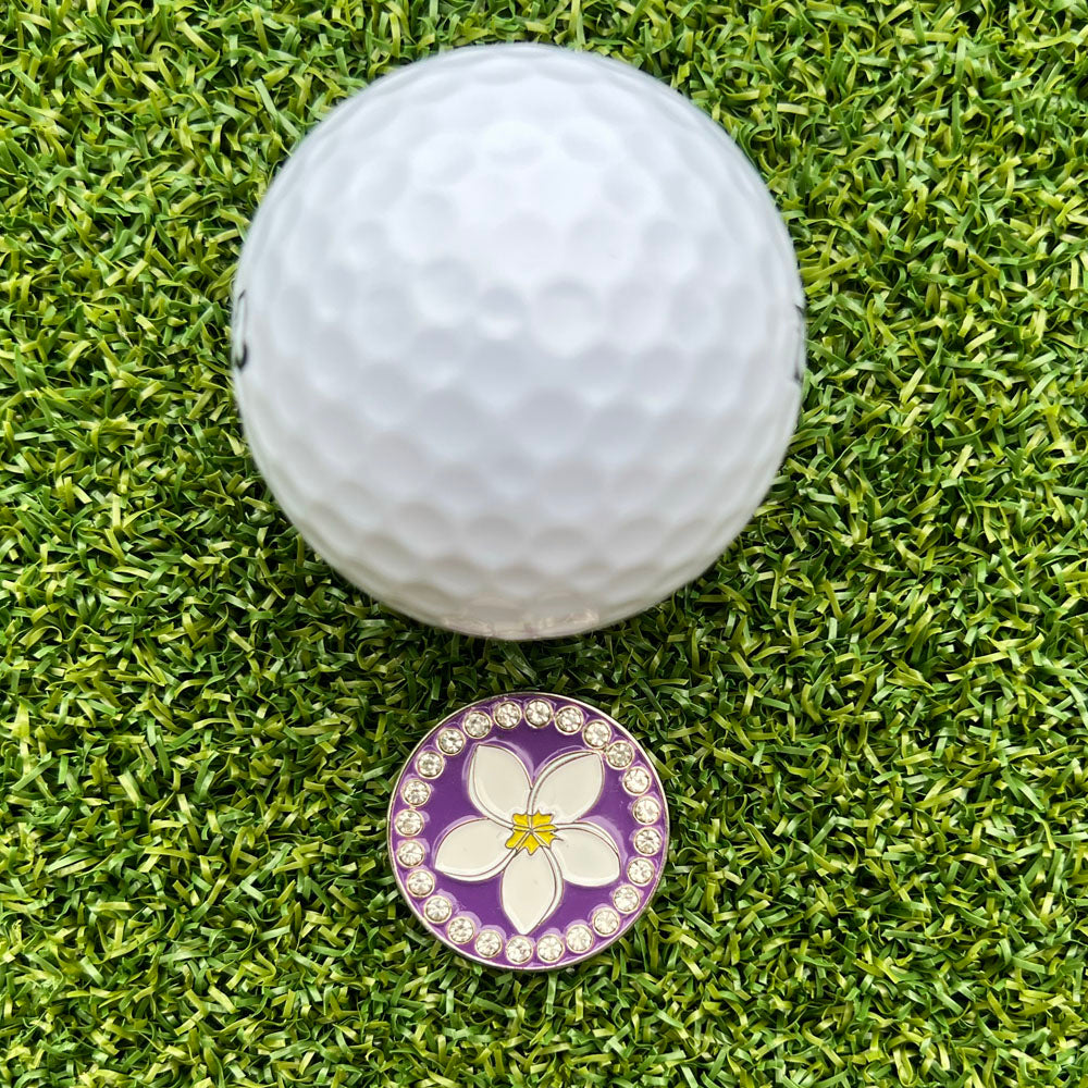 Golf ball on green grass with a decorative golf ball marker featuring a plumeria flower design.