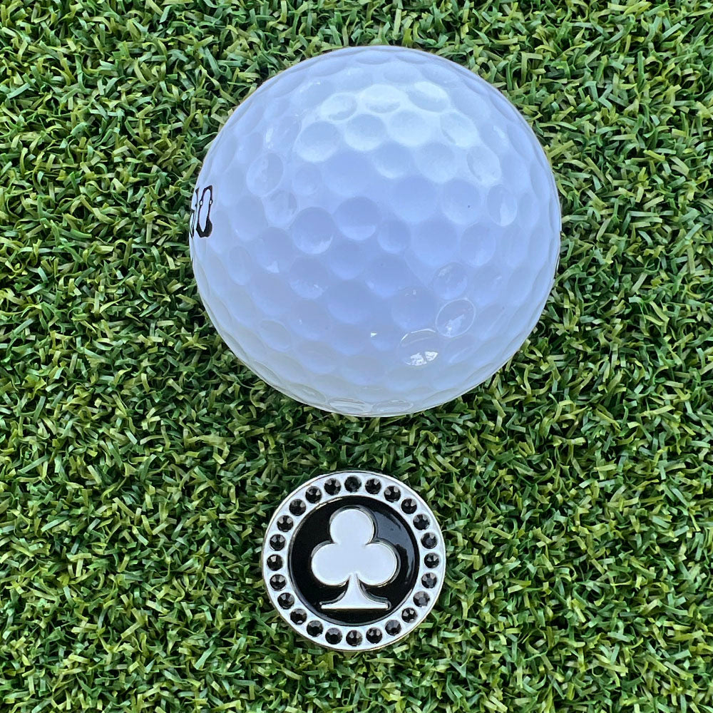 Golf ball on grass with a black and white poker club golf ball marker
