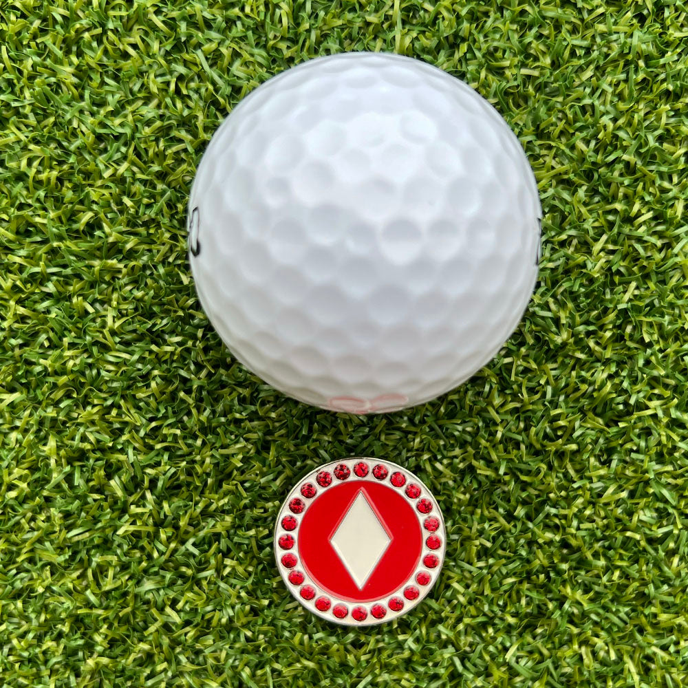 Golf ball on green grass with a red and white ball marker with diamond design