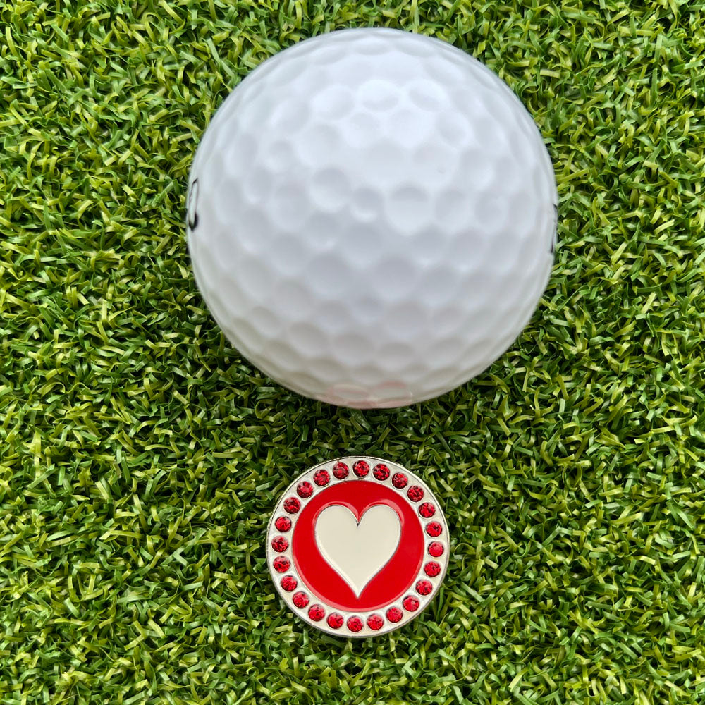 golf ball on grass with a red and white ball marker with heart design