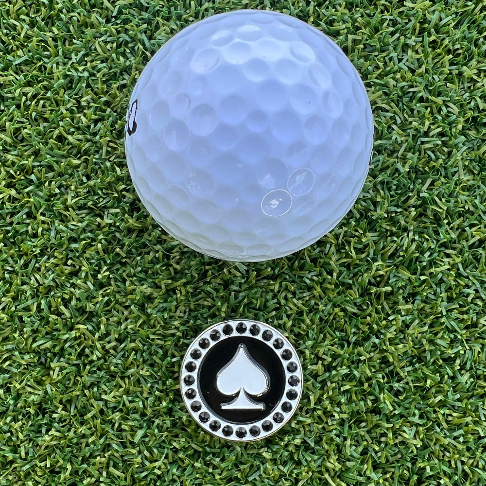 Golf ball on a green grass with a black and white poker spade golf ball marker